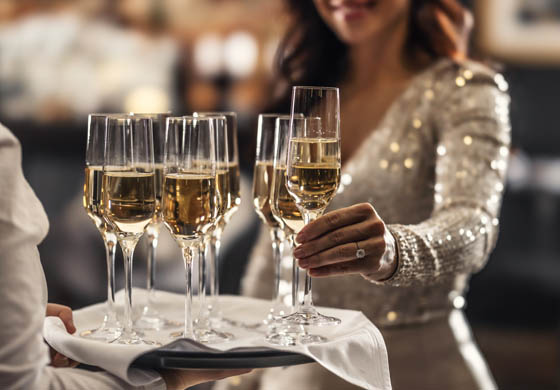 Close-up of woman in a sparkly dress reaching for a glass of champagne, being circulated by a waiter on a tray